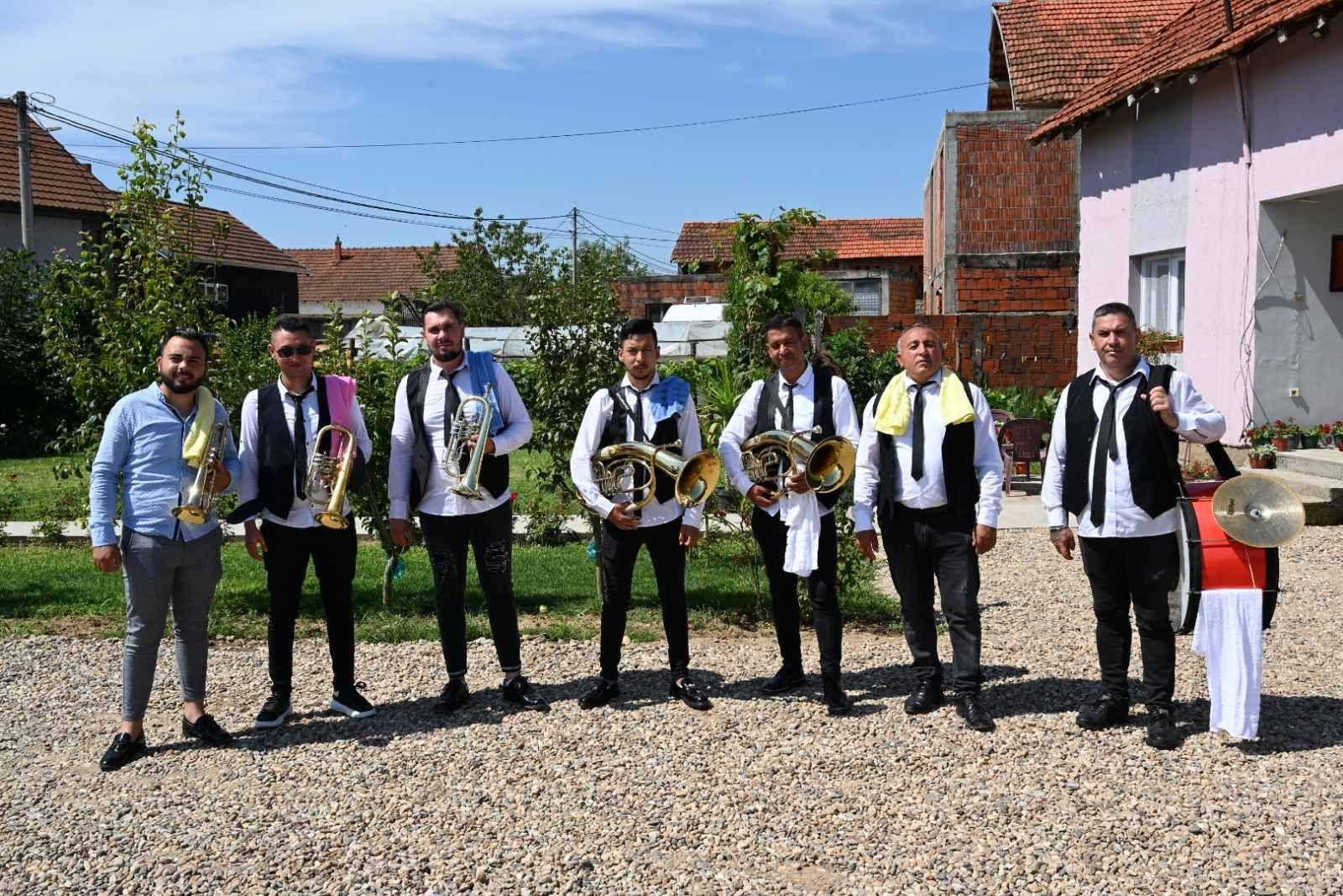 Group of musicians with brass instruments and drum standing outdoors on a sunny day.