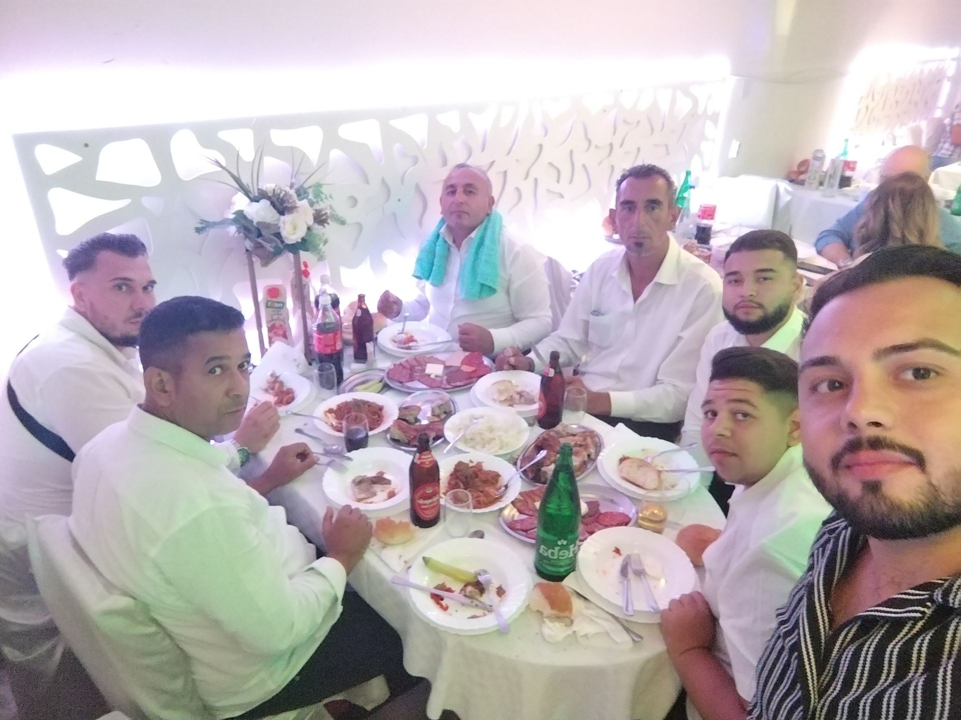 Group of men in white shirts sitting around a table with plates of food and soda bottles.