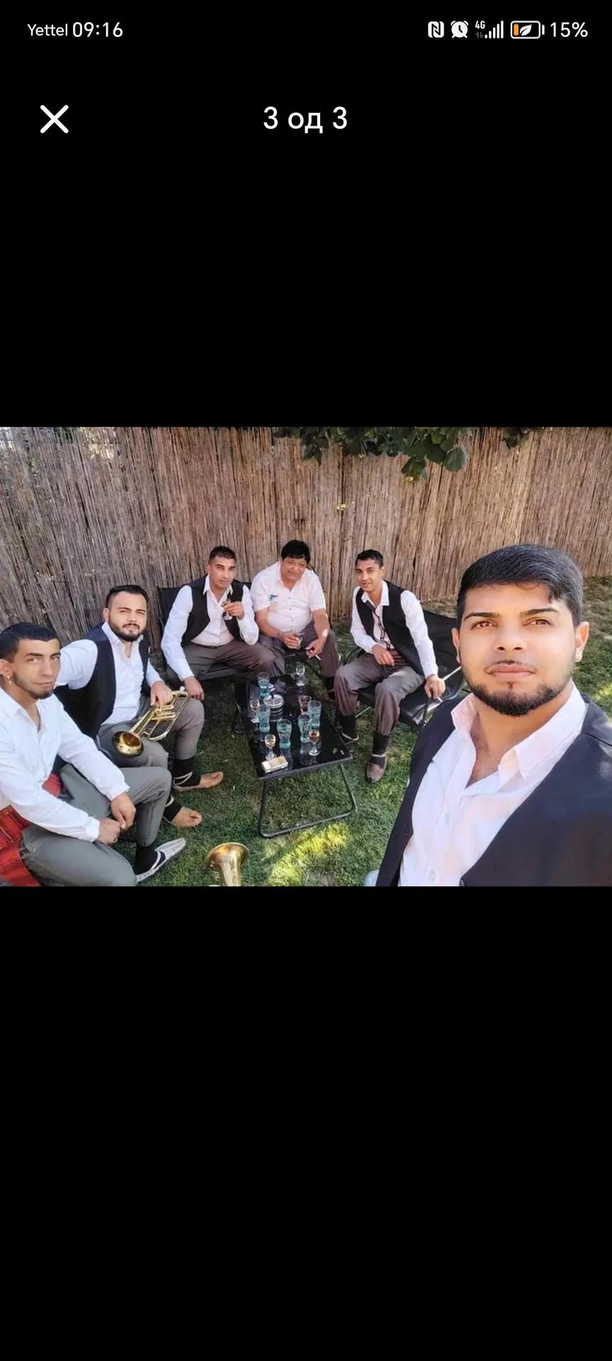 Group of men in formal attire sitting and standing around a table with drinks on a grassy lawn.